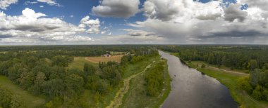 Polonya 'nın Nowy Lubiel kentindeki yemyeşil ve ormanlardan sakin bir nehir akar. Açık araziler ve küçük bir köy parçalı bulutlu bir gökyüzünün altında görünür..