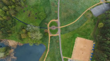 Litvanya, Druskininkai 'deki bir parkın havadan görünüşü, dairesel yollar, sazlıklarla dolu bir gölet, kumlu bir eğlence alanı ve yoğun ormanın çevresini gösteriyor..