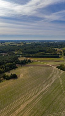 Parçalı bulutlu bir gökyüzü altında görünür traktör izleri ve yoğun orman parçalarıyla geniş alanlar, düz arazi ve tarımsal faaliyet sergiliyor.