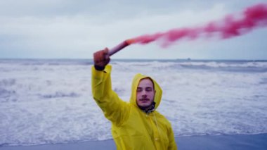 a portrait of a man in a yellow windbreaker gives a Emergency signall on the beach in a storm