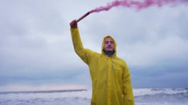 lonely man portrait on the beach in a yellow rain jumpsuit in his hand signal smoke