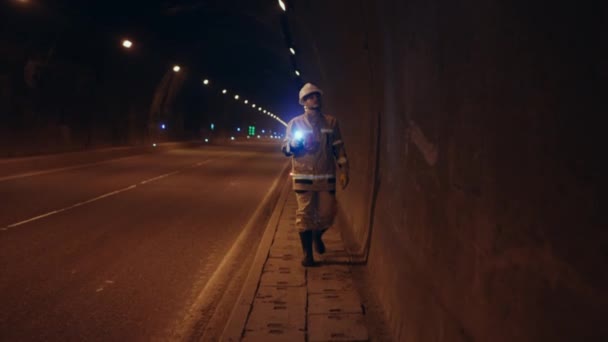 道路運送事業の労働者又は懐中電灯を手にヘルメットを被った技術者が車のトンネルの壁を検査する — ストック動画