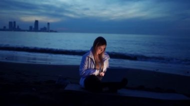 Kadın gece serbest çalışanı, akşamları deniz kıyısında dizüstü bilgisayar kullanıyor.