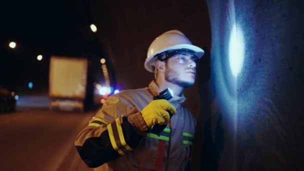 深刻で心配な男の肖像道路整備士が提灯を手にした車のトンネルの壁を検査する — ストック動画