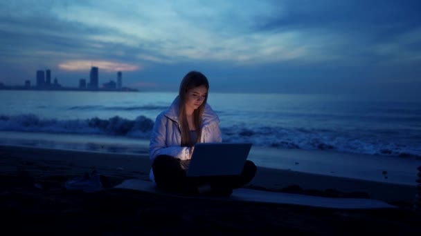 夜になると女性のフリーランサーが海の上にノートパソコンを使い — ストック動画