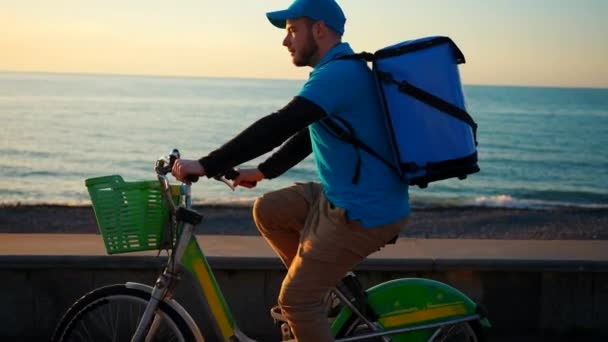 身穿蓝色制服 背着一背包食物的送货员 骑着自行车从侧面看去 — 图库视频影像