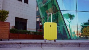 Modern cam binaların arka planında insanlar olmadan yalnız sarı bavul. Seyahat fikri.
