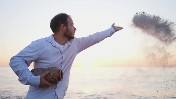 海の背景に手で灰を投げる男が閉じる — ストック動画