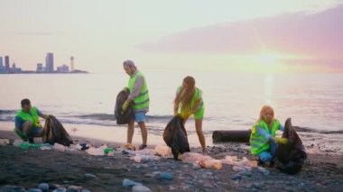 Gün batımında deniz kıyısını plastik çöpten temizleyen gönüllülerden oluşan pozitif bir ekip.