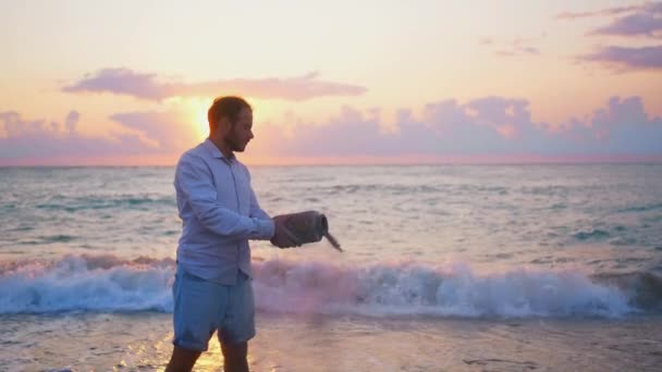 日没の美しい太陽の上で海の上の火葬から水に灰を散らす男 — ストック動画
