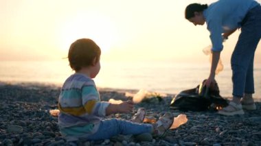 Gönüllü aile anne ve kızı okyanus kenarındaki plastik çöpleri topluyor.