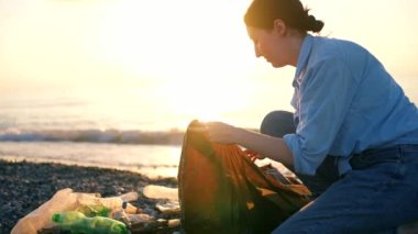 Orta yaşlı bir gönüllü gün batımında okyanusun kenarında plastik çöp topluyor.