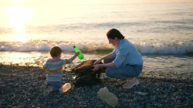 Bir anne ve küçük bir kız gönüllü olarak plastik okyanus plajı gün batımını topluyor.