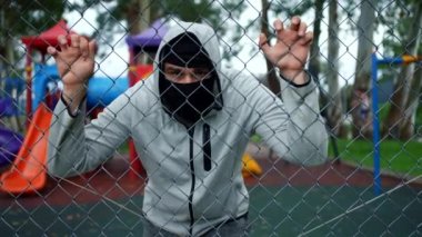 Çocuk parkında maskeli ve kapüşonlu bir adam izliyor.