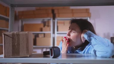 Bir depoda çalışan uykulu ve yorgun bir kadın.