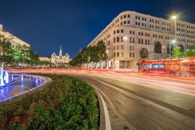 Ho Chi Minh, Viet Nam - 10 Nisan 2023: Saigon Belediye Binası, Vincom Merkezi kuleleri, muhteşem geceye karşı renkli sokak trafiği ve tropikal bitkiler. Saigon şehir merkezinin ünlü simgeleriyle.