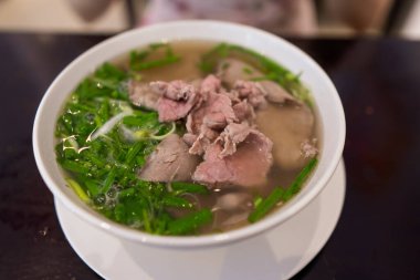 Vietnamca pho bo baharatlı çorba ya da beyaz seramik kasede pirinç eriştesi, sığır eti dilimleri ve ahşap arka planda bitkiler. Kuzey Vietnam halkının zevkine ve tarzına göre pişirildi.