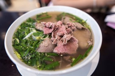 Vietnamca pho bo baharatlı çorba ya da beyaz seramik kasede pirinç eriştesi, sığır eti dilimleri ve ahşap arka planda bitkiler. Kuzey Vietnam halkının zevkine ve tarzına göre pişirildi.