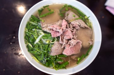 Vietnamca pho bo baharatlı çorba ya da beyaz seramik kasede pirinç eriştesi, sığır eti dilimleri ve ahşap arka planda bitkiler. Kuzey Vietnam halkının zevkine ve tarzına göre pişirildi.