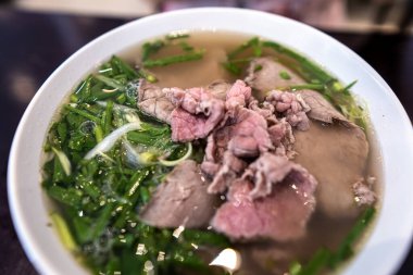 Vietnamca pho bo baharatlı çorba ya da beyaz seramik kasede pirinç eriştesi, sığır eti dilimleri ve ahşap arka planda bitkiler. Kuzey Vietnam halkının zevkine ve tarzına göre pişirildi.