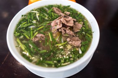 Vietnamca pho bo baharatlı çorba ya da beyaz seramik kasede pirinç eriştesi, sığır eti dilimleri ve ahşap arka planda bitkiler. Kuzey Vietnam halkının zevkine ve tarzına göre pişirildi.