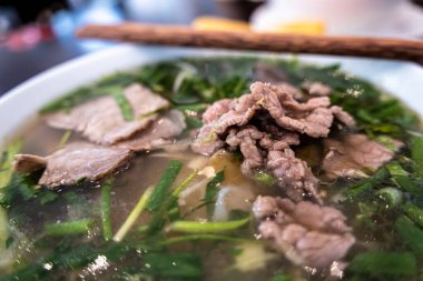 Vietnamca pho bo baharatlı çorba ya da beyaz seramik kasede pirinç eriştesi, sığır eti dilimleri ve ahşap arka planda bitkiler. Kuzey Vietnam halkının zevkine ve tarzına göre pişirildi.