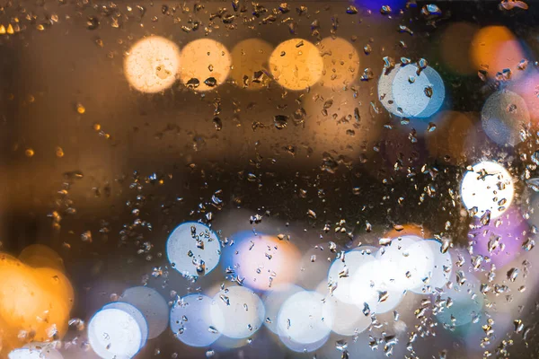 City view through the window on a rainy night, Rain falling on the window with light effect on the road, City life at night in rainy season abstract background. Focus on the drop on the glass