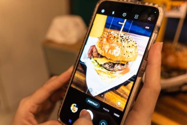 Fast food yiyen bir kadın akıllı telefon çekiyor. Lezzetli ev yapımı hamburgerler.