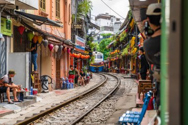 Hanoi, Vietnam - 27 Haziran 2024: Hanoi 'nin Eski Mahallesi' ndeki dar bir sokaktan bir tren geçiyor. Turistler hızlı trenin fotoğraflarını çeker. Hanoi 'nin Tren Sokağı popüler bir turistik merkezdir..