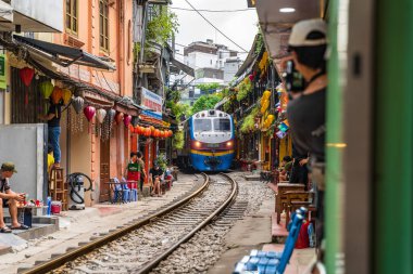 Hanoi, Vietnam - 27 Haziran 2024: Hanoi 'nin Eski Mahallesi' ndeki dar bir sokaktan bir tren geçiyor. Turistler hızlı trenin fotoğraflarını çeker. Hanoi 'nin Tren Sokağı popüler bir turistik merkezdir..