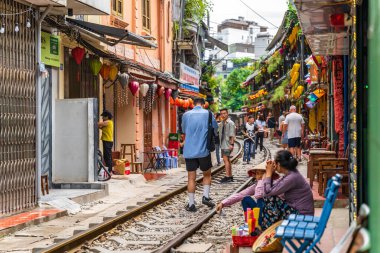 Hanoi, Vietnam - 27 Haziran 2024: Hanoi 'nin Eski Mahallesi' ndeki dar bir sokaktan bir tren geçiyor. Turistler hızlı trenin fotoğraflarını çeker. Hanoi 'nin Tren Sokağı popüler bir turistik merkezdir..