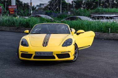 Hanoi, Vietnam - 26 Haziran 2024: Hanoi, Vietnam 'da sokağa park edilmiş sarı bir Porsche 718 Boxster. Porsche, 1931 'de kurulan yüksek performanslı spor arabalar konusunda uzman bir Alman otomobil üreticisi..