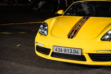 Hanoi, Vietnam - 26 Haziran 2024: Hanoi, Vietnam 'da sokağa park edilmiş sarı bir Porsche 718 Boxster. Porsche, 1931 'de kurulan yüksek performanslı spor arabalar konusunda uzman bir Alman otomobil üreticisi..