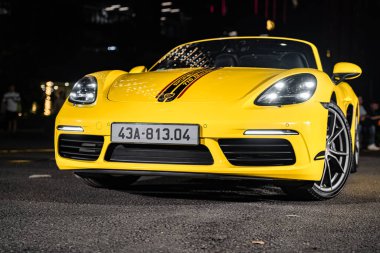 Hanoi, Vietnam - 26 Haziran 2024: Hanoi, Vietnam 'da sokağa park edilmiş sarı bir Porsche 718 Boxster. Porsche, 1931 'de kurulan yüksek performanslı spor arabalar konusunda uzman bir Alman otomobil üreticisi..
