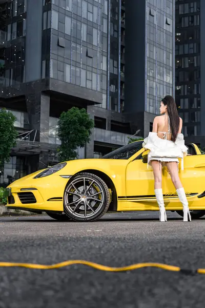Hanoi, Vietnam - 26 Haziran 2024: Porsche 718 Boxster ile bikini giyen güzel genç bir kadın moda fotoshoot sırasında sokağa park etmiş. Porsche, 1931 'de kurulan yüksek performanslı spor arabalar konusunda uzman bir Alman otomobil üreticisi..
