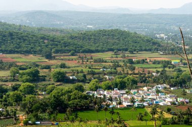 Güzel bir tepe manzaralı tarım arazisi ve küçük bir köy. Tarım arazisi yemyeşil ve köy de bir vadiye yerleşmiş. Güneş ışıl ışıl parlıyor ve gökyüzü açık mavi..