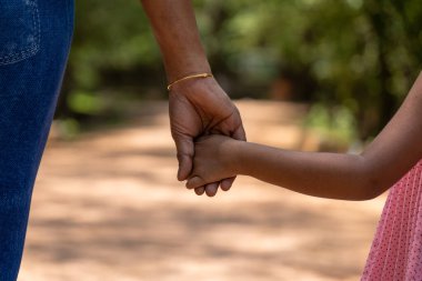 Küçük bir kız ve annesi parkta hassas bir anı paylaşıyorlar. Kızın minicik eli annesinin elini sıkıca kavrayıp sevgi ve güven saçan bir bağ kuruyor..