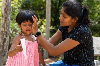 Küçük bir kız elinde bir roket tutuyor, neşe ve heyecanla parıldıyor. Annesi yanında duruyor, kızının mutluluğunu izlerken günün yorgunluğunu siliyor..