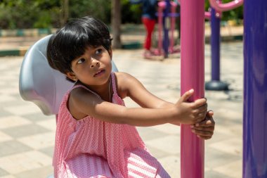 Küçük bir kız neşeli bir çocuk parkında renkli oyun ekipmanlarını keşfediyor..