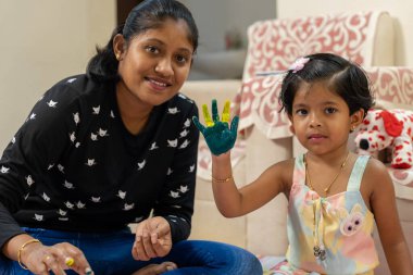 Bu resim, küçük bir kızın yeşil ve sarıya boyanmış elini gösteriyor ve gülümsüyor.