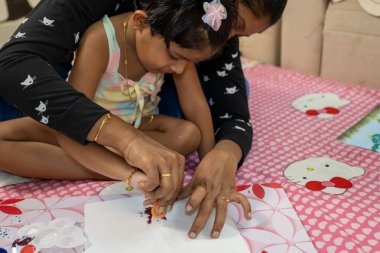 Bu resim, anne ve kızının sünger ve kızının kucağına oturup resim yapmalarıyla ilgili.