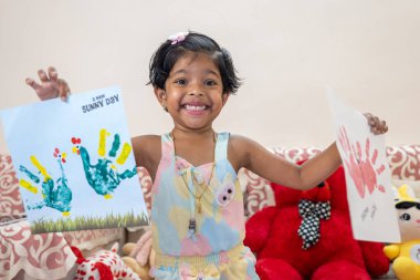 Bu resim, Küçük Çocuk 'un resim kağıdını göstermesiyle ilgili. Resim, gülümseyen ve boyama kağıdının keyfini çıkaran çocuk tarafından renklendirilmiş.