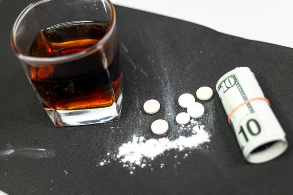 A close-up photo of drugs, tablets, dollar bills, and alcohol on a plain background. The photo conveys the sense of addiction and the negative consequences of drug use.