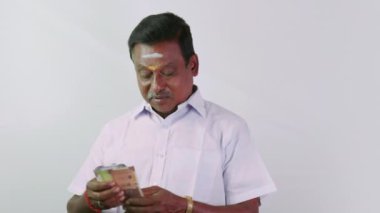 Bu video, beyaz gömlek ve dhoti rupi 'ye para sayan ve ayarlayan Güney Hintli bir adam hakkında.