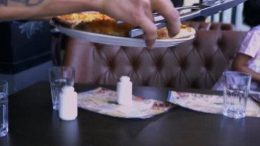 Bu video sunucu elinde bıçak ve kaşık dövmesiyle masada pizza servisi yapmakla ilgili.