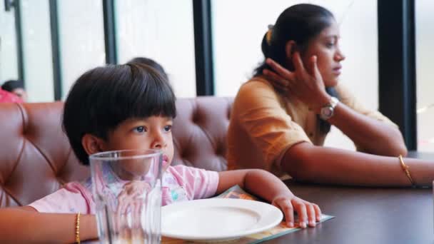 这段视频讲的是妈妈和女儿在酒店咖啡店里等食物 孩子们穿着粉色衣服 玻璃杯和盘子在她面前 — 图库视频影像