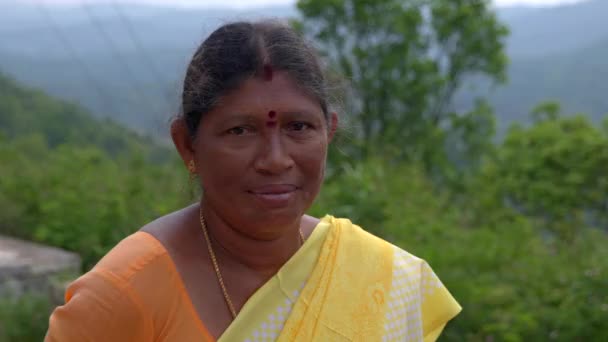 一个印度老妇人在镜头前微笑的画像 这名妇女穿着传统的印度服装 有一头长长的黑头发 背景是一片树木丛生的森林 — 图库视频影像