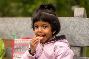 Parktaki bankta oturan tatlı genç bir kız lezzetli bir bisküvinin tadını çıkarıyor. Gülümsüyor ve kameraya bakıyor.