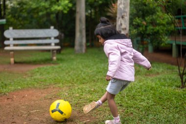 Bu stok fotoğrafı parkta futbol oynayan neşeli bir genç kızı gösteriyor. Güneş parlıyor ve çimenler yeşil. Fotoğraf, futbol kulüpleri, spor giyim markaları veya çocuk ürünleri için pazarlama materyallerinde kullanılmak üzere mükemmel..