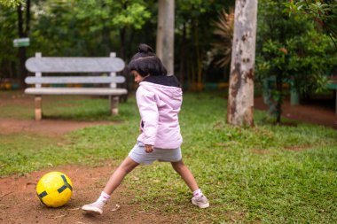 Genç bir kız parkta futbol topunu tekmelemeden önce bacağını esnetir..